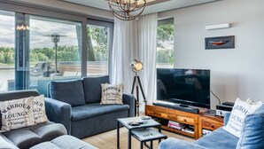 A modern living room with a large TV, comfortable seating, and a view of the outdoors.