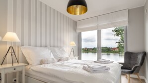 A modern bedroom with a large bed, two bedside lamps, a chair, and a view of a lake.