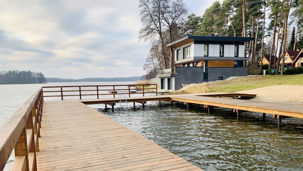 A wooden dock extending into a lake with a modern house in the background.