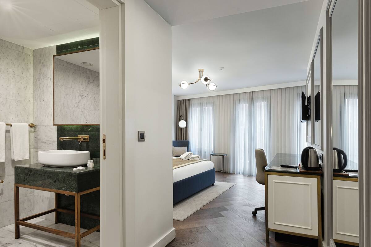Une chambre d’hôtel moderne avec une salle de bain en marbre, un grand lit, un bureau et une vue sur la ville.