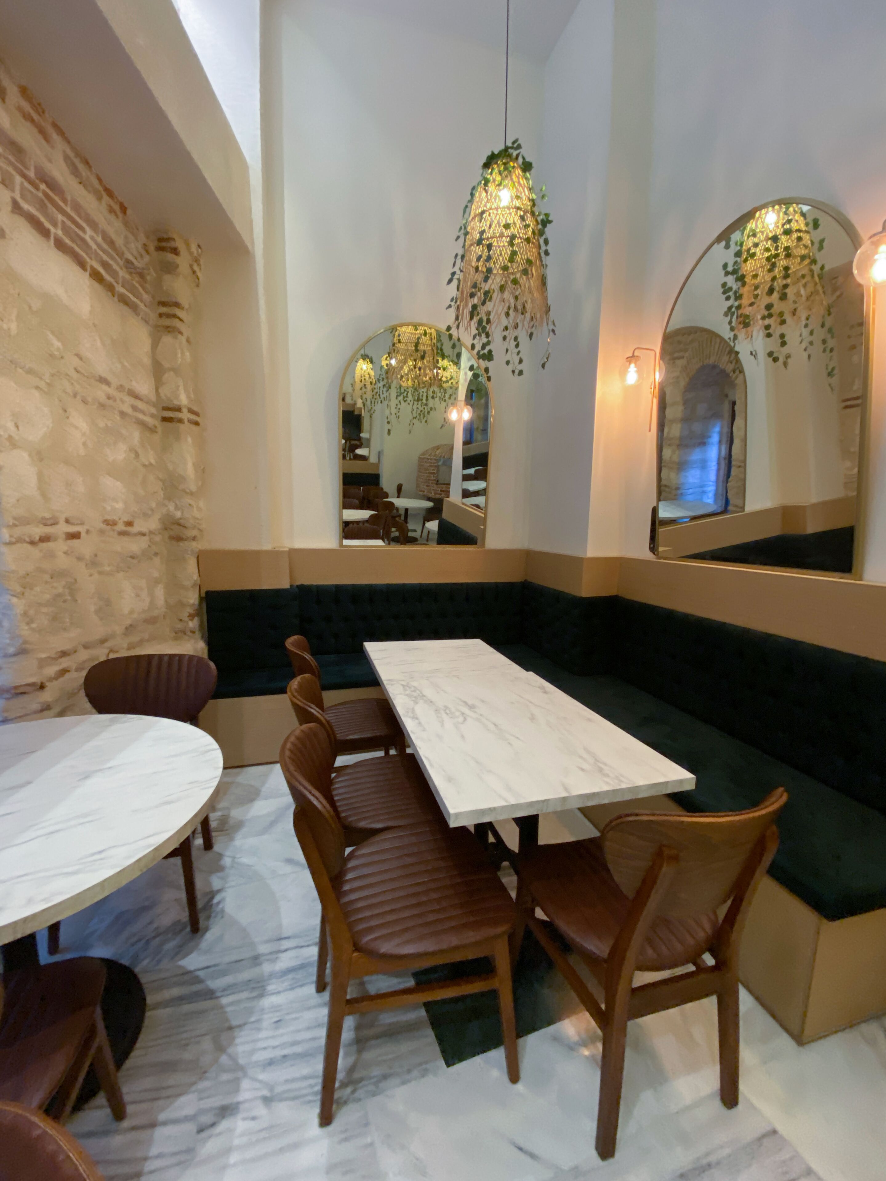 Een restaurantinterieur met een marmeren tafel, houten stoelen, een groene bank en hangende planten.