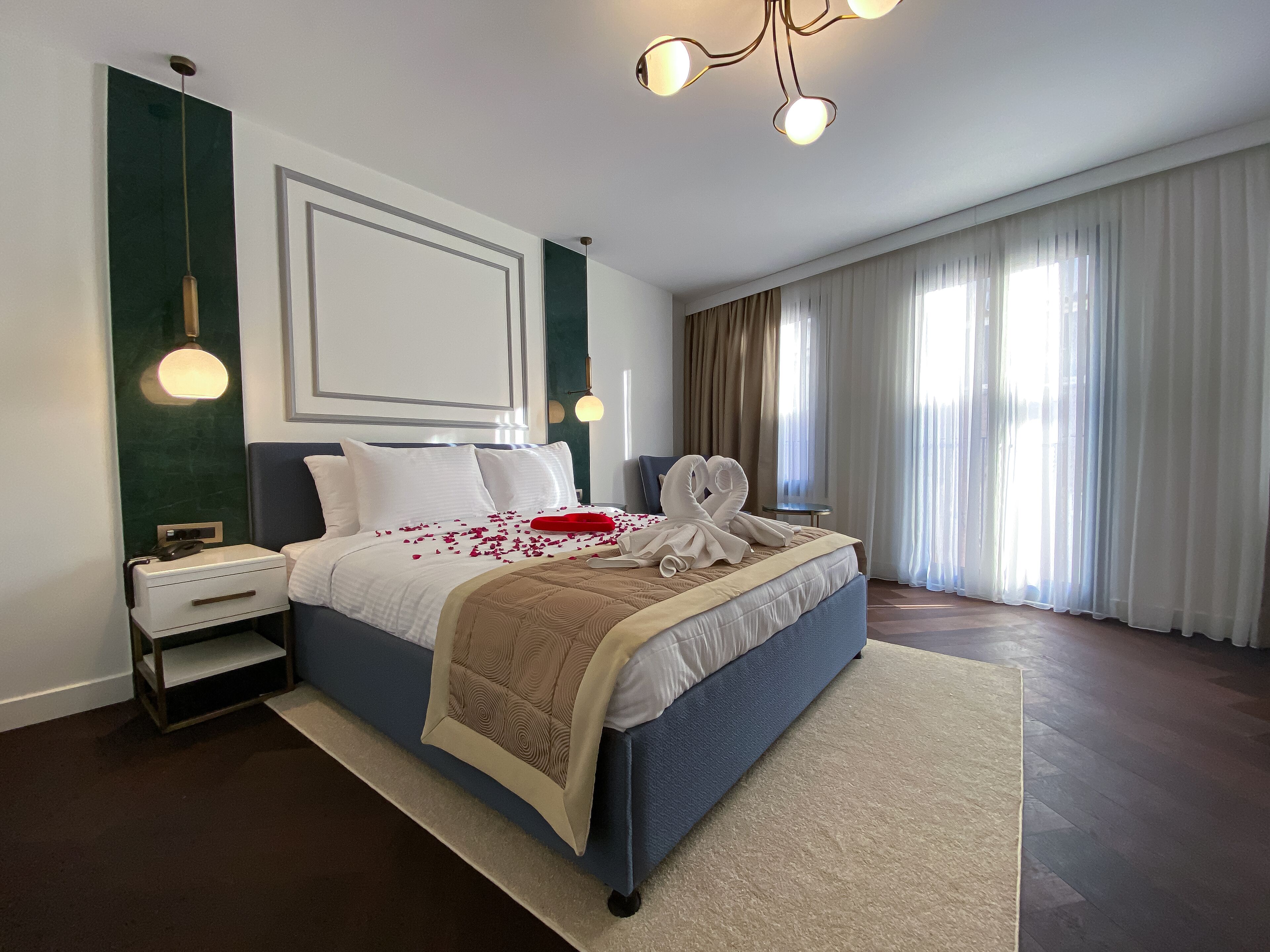 Una habitación de hotel moderna con una cama grande, una mesita de noche y un amplio ventanal con cortinas.