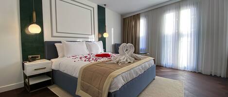 Una habitación de hotel moderna con una cama grande, una mesita de noche y un amplio ventanal con cortinas.