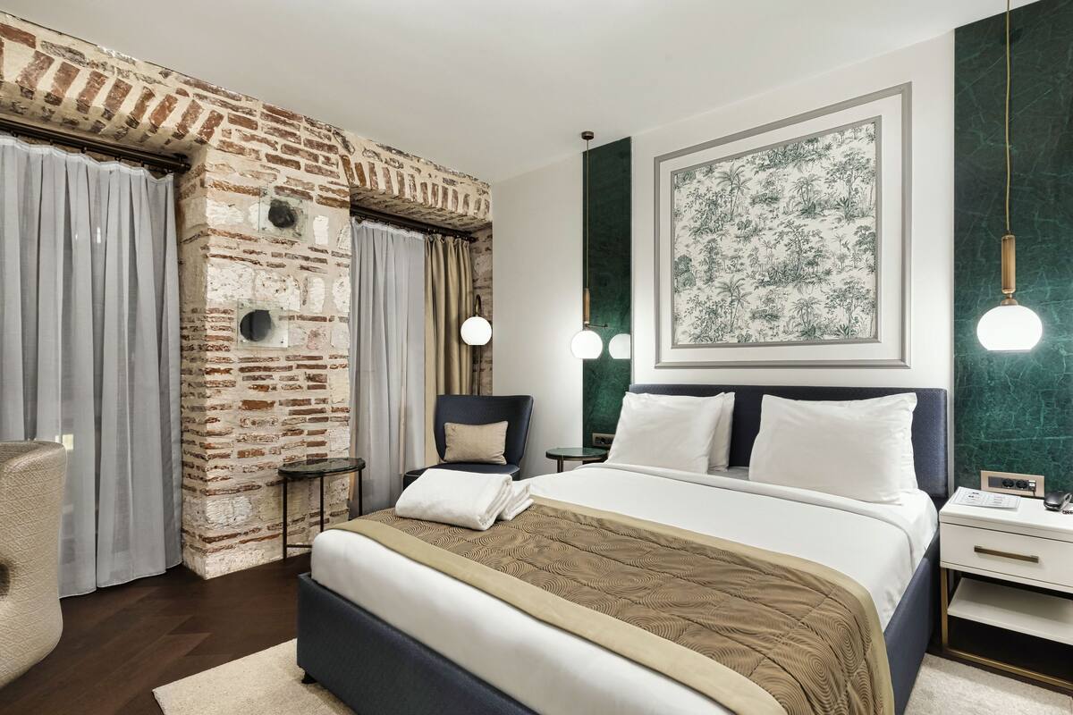 Une chambre moderne avec un mur en briques, un grand lit avec du linge de lit blanc, une tête de lit bleu foncé et un mur d’accent vert.