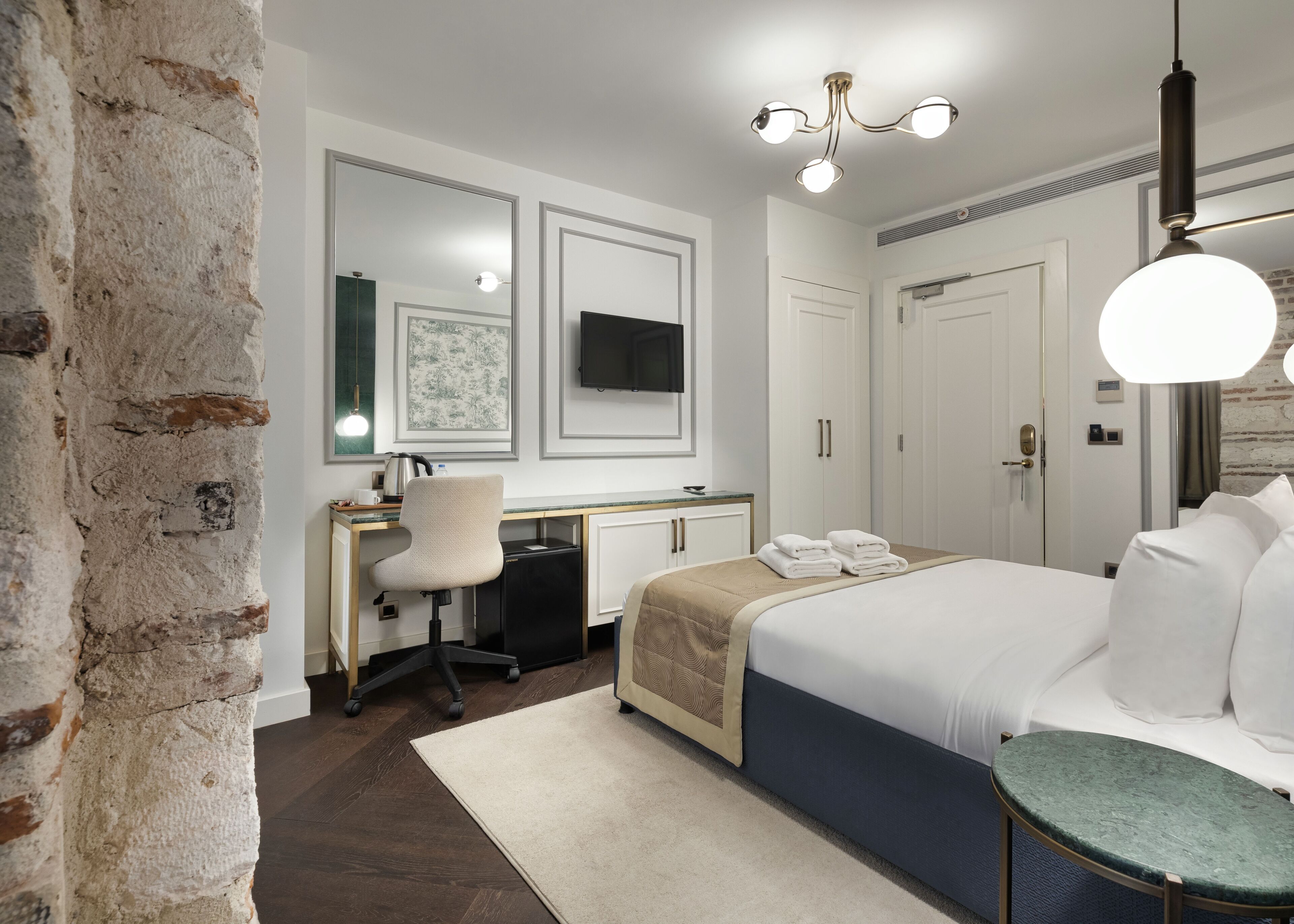 A modern hotel room with a bed, desk, chair, and a large mirror.