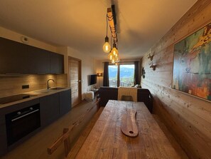 A modern kitchen with a wooden dining table, built-in appliances, and a view of the outdoors.