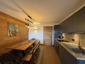 A modern kitchen with a wooden dining area, a built-in stove, and a hanging light fixture.