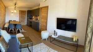 Ett modernt vardagsrum med en soffa, ett soffbord, en tv och en matplats med stolar och ett bord.