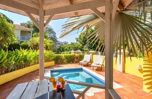 Un espace piscine agrémenté d’une pergola, de chaises longues et d’une table où sont servis des boissons.