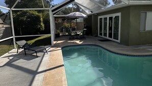 Une piscine extérieure couverte avec un espace patio comprenant des chaises longues et une table.
