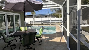 Un patio couvert avec une piscine, du mobilier d’extérieur et une vue sur le jardin arrière.
