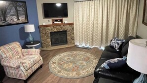 A living room with a stone fireplace, a television, a patterned rug, a sofa, and a couch. - Riverside Condo w/ Deck (Pigeon Forge)