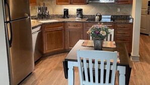 A modern kitchen with wooden cabinets, stainless steel appliances, and a white dining table with a chair. - Riverside Condo w/ Deck (Pigeon Forge)