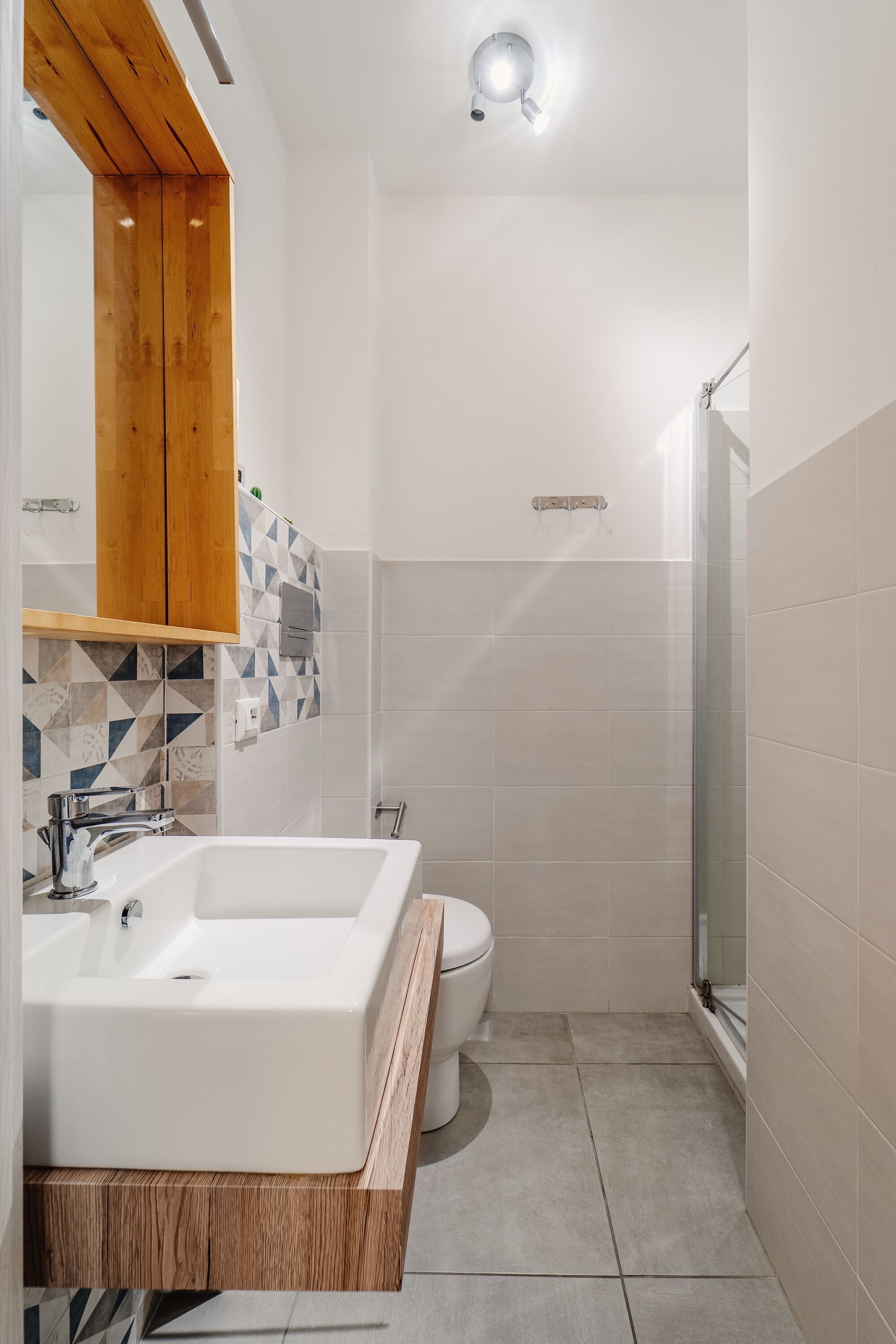 Un bany modern amb un envàs de paret blanc gran, un penjador de fusta, un vàter i una cabina de dutxa de vidre.