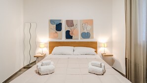 Ein ordentlich bezogenes Bett mit zwei Handtüchern, einem Holz-Kopfteil und drei Wandleuchten.