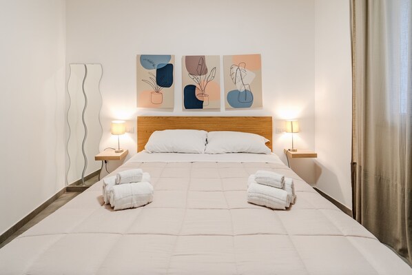 A neatly made bed with two towels, a wooden headboard, and three wall-mounted lamps.