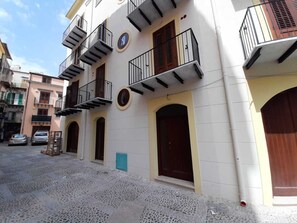 Un immeuble à plusieurs étages, doté de balcons, d’une porte centrale et d’une petite fenêtre bleue.