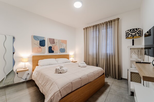 Une chambre d’hôtel avec un lit, des lampes de chevet, un bureau, une télévision et des œuvres d’art accrochées au mur.