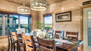 Un intérieur en bois avec une table à manger dressée pour six personnes, de grandes fenêtres et un lustre.
