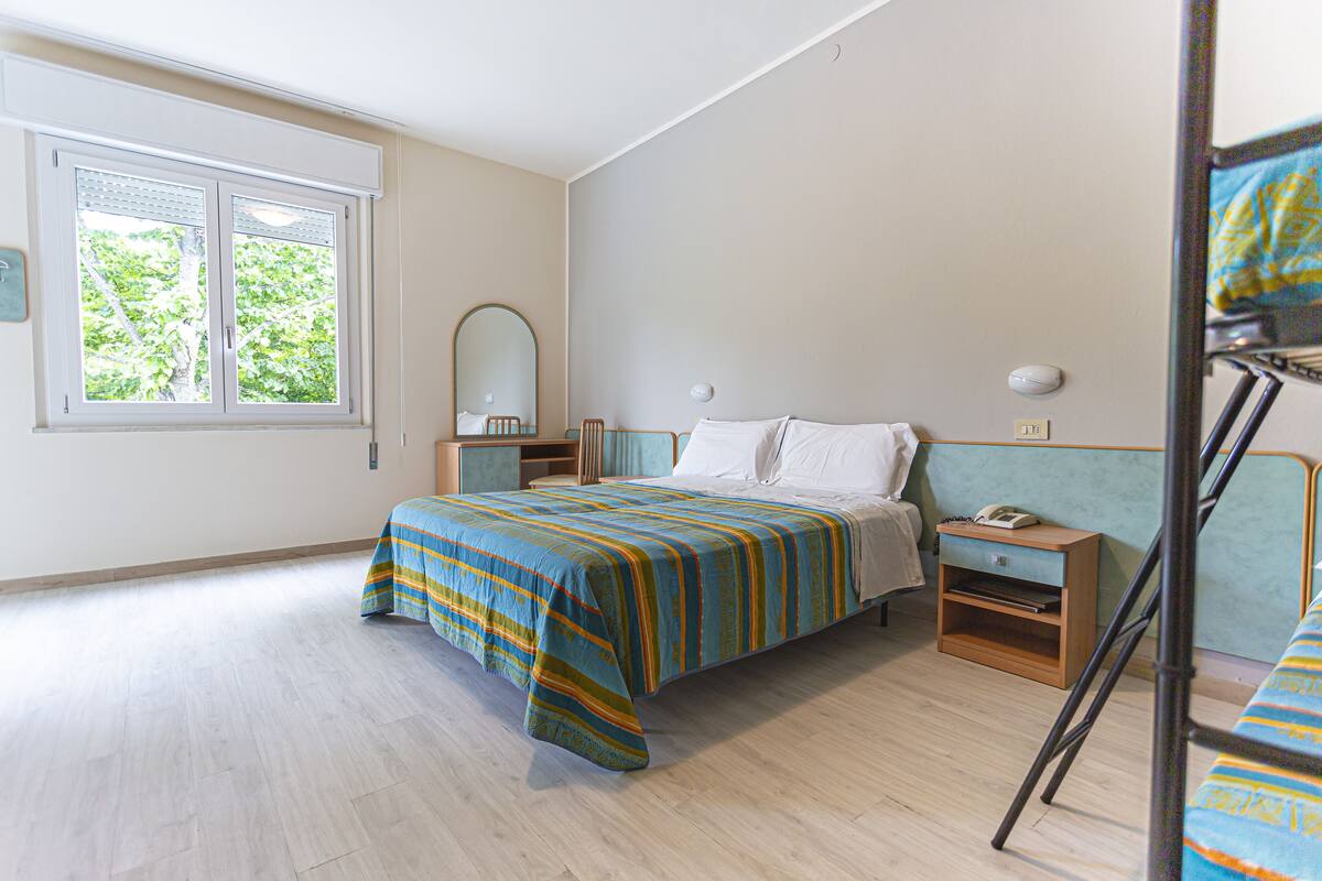 Een slaapkamer met een bed, nachtkastje, spiegel en een raam met jaloezieën.