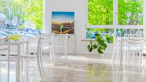A bright room with white furniture, a large window with a view of trees and parked cars, and a painting on the wall.