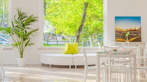 A bright room with a large window, a white sofa with a yellow pillow, a potted plant, and a table with chairs.