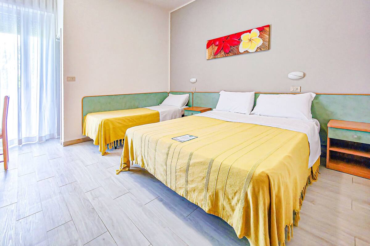 Een hotelkamer met twee eenpersoonsbedden, een groot bed, een schilderij aan de muur en een houten vloer.