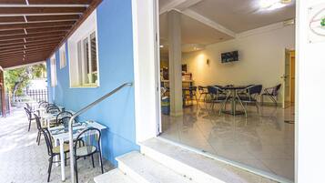 A covered outdoor seating area with tables and chairs, a staircase leading to an indoor space, and a television mounted on the wall.