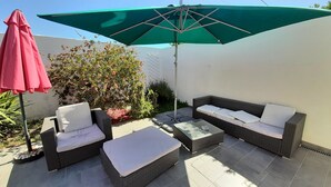 Une terrasse extérieure avec des meubles en osier, un parasol vert et un parasol rouge.