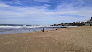 Une plage avec un phare en arrière-plan, un rivage sablonneux et quelques personnes.