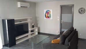 Un salon moderne avec un téléviseur à écran plat, un canapé gris agrémenté d’un coussin jaune, une table basse en verre et un tableau représentant un lion accroché au mur.