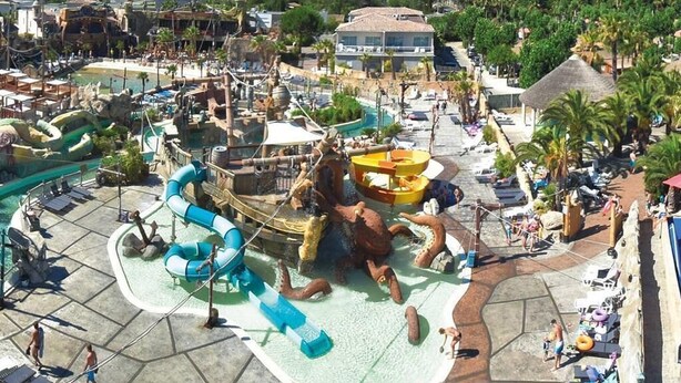 Un parc aquatique avec des toboggans, une grande statue de poulpe et des chaises de plage.