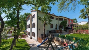 A multi-story building with a playground area, including a slide and climbing structure, surrounded by greenery and a clear sky. - Holiday apartment with pool and air conditioning (Poreč)