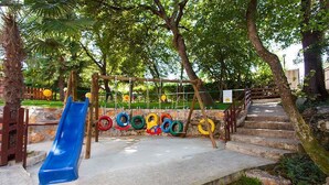 A playground with a blue slide, a rope swing, and a set of colorful tires hanging from a wooden structure. - Holiday apartment with pool and air conditioning (Poreč)