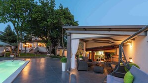 A modern outdoor patio with a pool, seating area, and a covered section with a fireplace. - Holiday apartment with pool and air conditioning (Poreč)