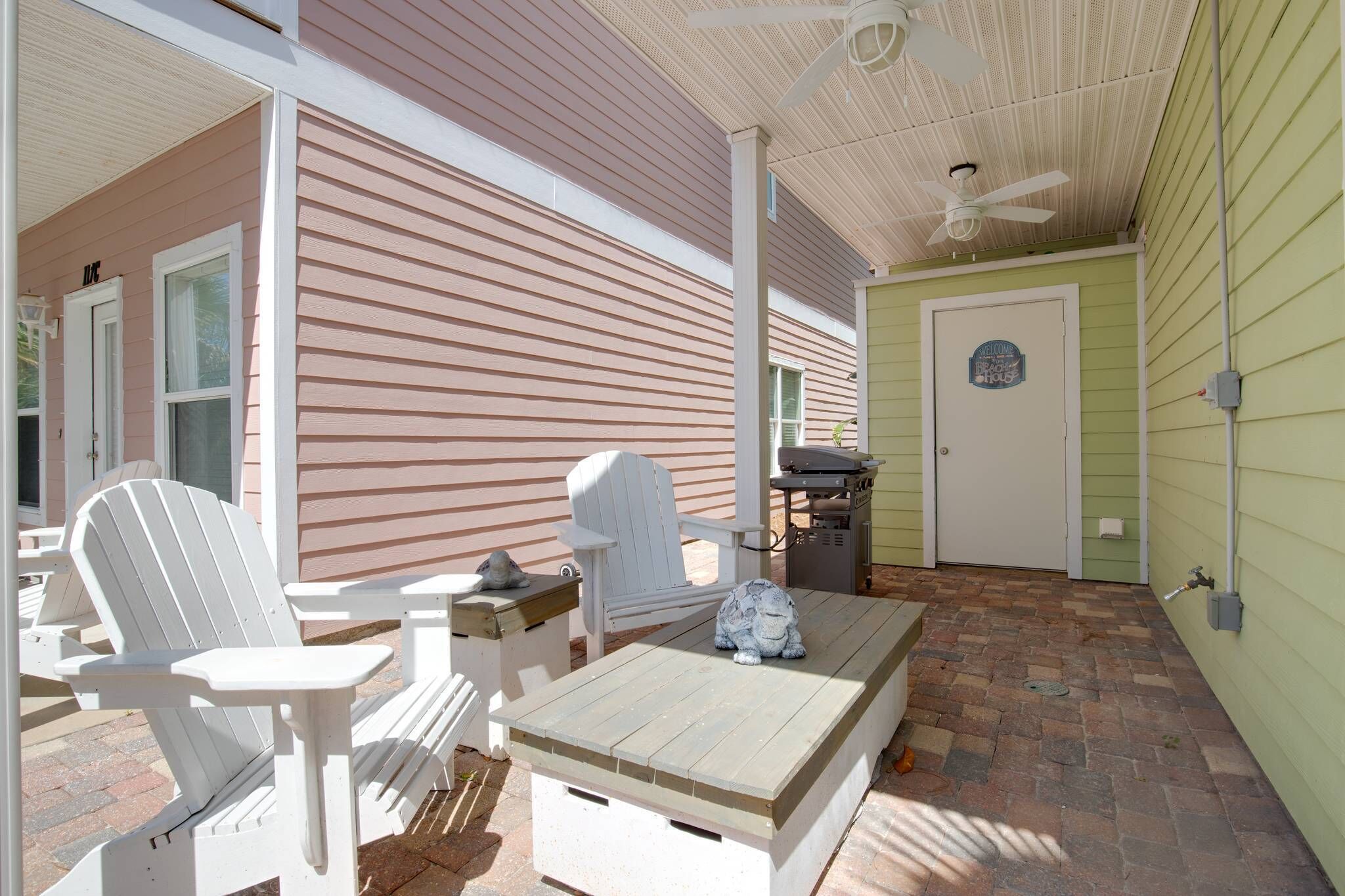 An outdoor patio with Adirondack chairs, a wooden table, and a grill.