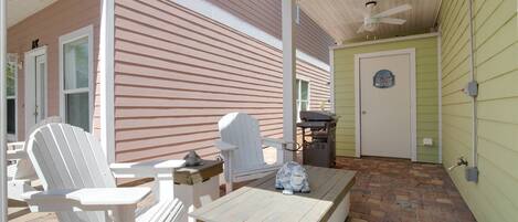 An outdoor patio with Adirondack chairs, a wooden table, and a grill.