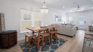 A modern living room with a wooden dining table, benches, a chandelier, and a ceiling fan. - Laguna Beach PCB 5/3, STEPS TO THE BEACH-5 STAR RENTAL- CONVENIENT TO EVERYTHING (PANAMA CITY BEACH)