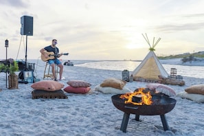 Une scène de plage avec une personne jouant de la guitare, un tipi et un foyer.