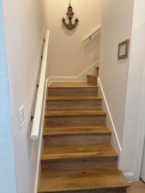 Un escalier en bois avec des rampes blanches, un luminaire fixé au mur et une petite plaque.