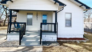 A small, single-story house with a gabled roof, a front porch with a black railing, and a mailbox. - Near St. Joseph Hospital - Large Fenced Lot W/ W&D (Wichita)
