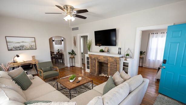 A living room with a sofa, coffee table, and a fireplace. There is a television mounted on the wall and a blue door. - Near St. Joseph Hospital - Large Fenced Lot W/ W&D (Wichita)