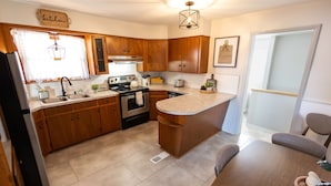 A modern kitchen with wooden cabinets, a central island, and a dining area with a table and chairs. - Near St. Joseph Hospital - Large Fenced Lot W/ W&D (Wichita)