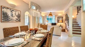A dining area with a long table set for a meal, a chandelier, and a staircase in the background. - Woodlands Luxury Villas (St Peter)