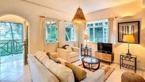 A living room with a sofa, TV, and a hanging light fixture. - Woodlands Luxury Villas (St Peter)