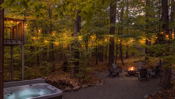 A forested area with a hot tub, outdoor seating, and string lights. - Pocono Lake Chalet w/Hot Tub, Pool Table, & Fire Pit. Pet friendly! (Pocono Lake)
