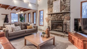 A cozy living room with a stone fireplace, a large window, and a television. - Pocono Lake Chalet w/Hot Tub, Pool Table, & Fire Pit. Pet friendly! (Pocono Lake)