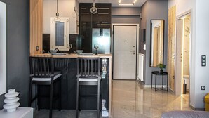 Una cucina moderna con isola centrale, due sgabelli da bar, illuminazione a sospensione e vista sul soggiorno comunicante.