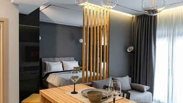 Una moderna camera d'albergo con un tavolo da pranzo in legno, un letto con biancheria grigia, un divano e una grande finestra con tende.