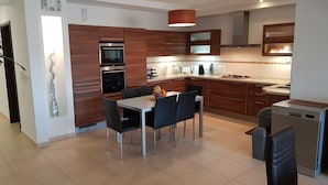 Eine moderne Küche mit Holzschränken, Edelstahlgeräten und einem Essbereich mit Tisch und Stühlen.